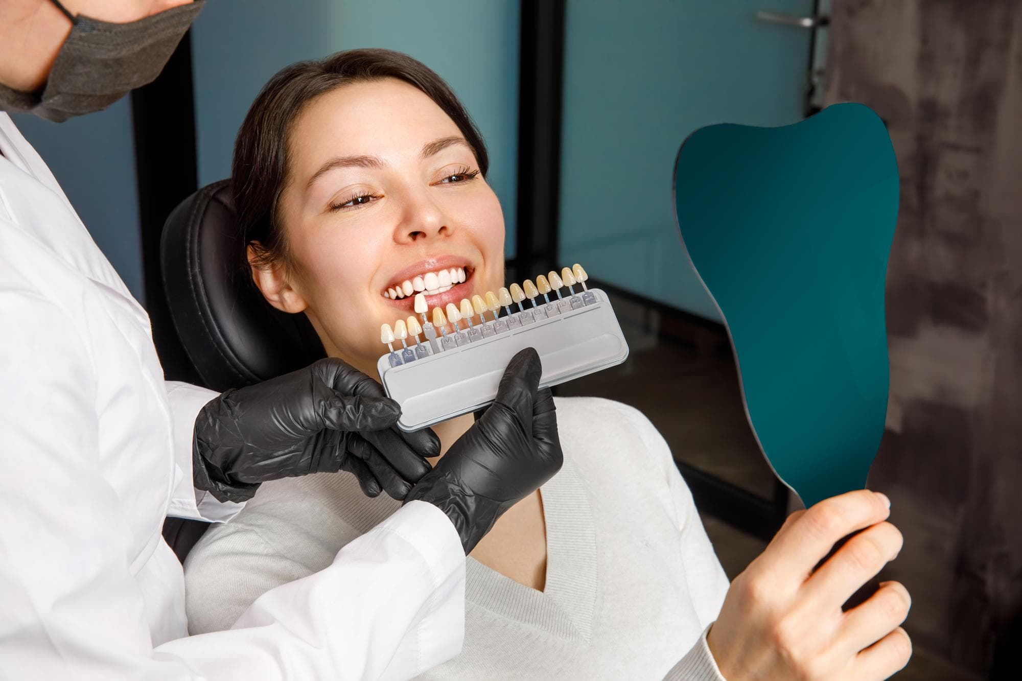 Dentist matching tooth shades for a smiling patient holding a mirror